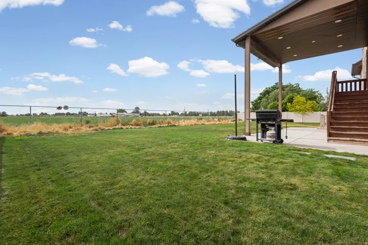 Expansive grass lawn with a covered concrete patio, wood deck, and chain link fencing