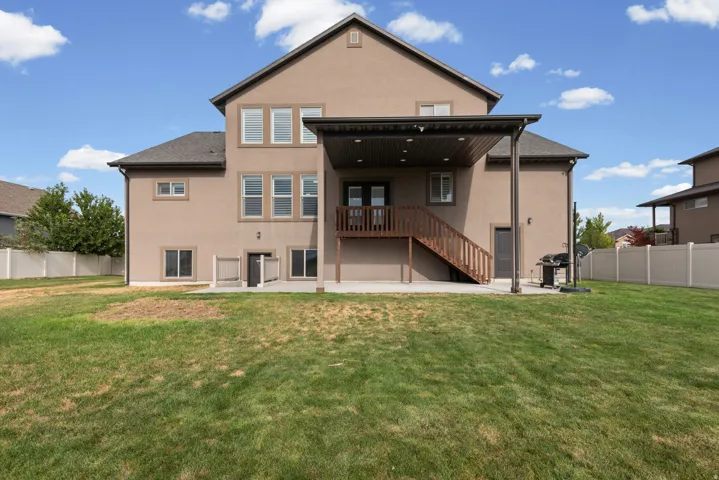 Expansive backyard featuring a covered patio, upper-level deck with wood railing, and a full-height privacy fence