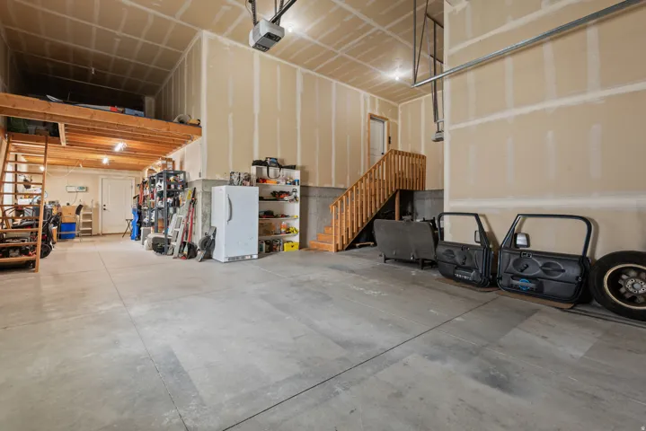 Garage with concrete flooring, natural wood staircase, wood-finish overhead storage, high ceilings, and recessed lighting
