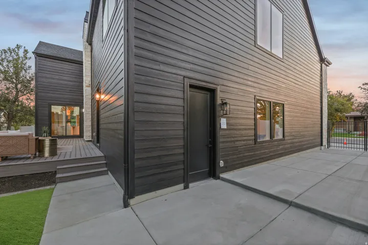 Black horizontal siding with stone accents, concrete patio, and dark wood-finish deck