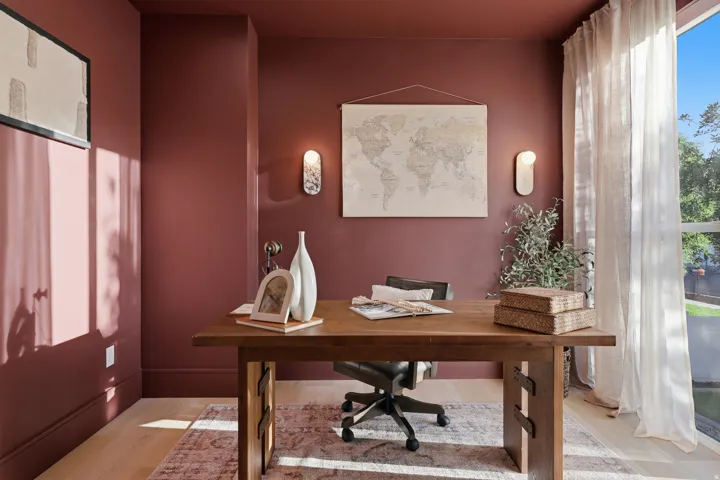 Hardwood flooring, large window with sheer drapery, two wall-mounted sconces, and a solid wood table