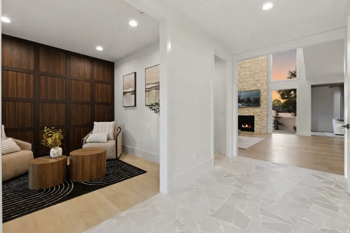 Stone tile flooring, wood-finish panel wall, recessed lighting, stone-clad fireplace, and large windows