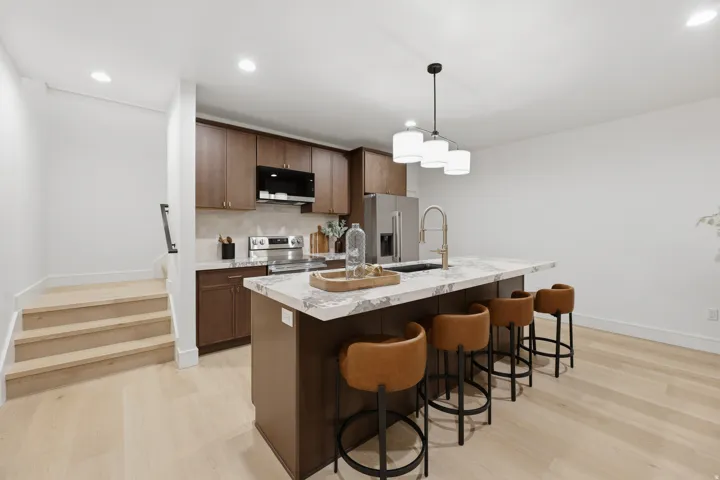 Kitchen featuring wood-finish flooring, dark wood cabinetry, white countertops, stainless steel appliances, and a central island with an attached sink