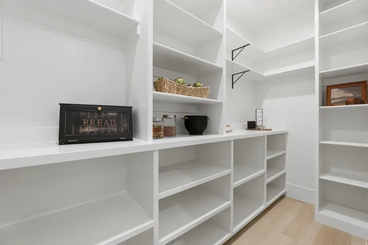 Expansive pantry with extensive white built-in shelving, durable white countertops, and light wood-finish flooring