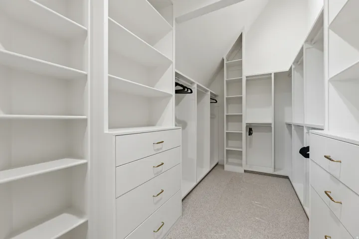 Built-in custom cabinetry with shelving, drawers with brass hardware, and hanging rods