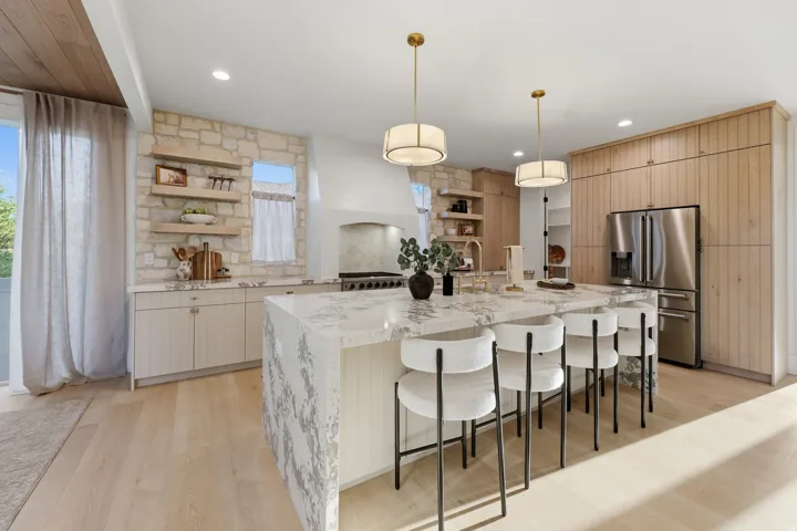 Gourmet kitchen featuring a stone accent wall, custom cabinetry, a waterfall island with a substantial countertop, and recessed lighting
