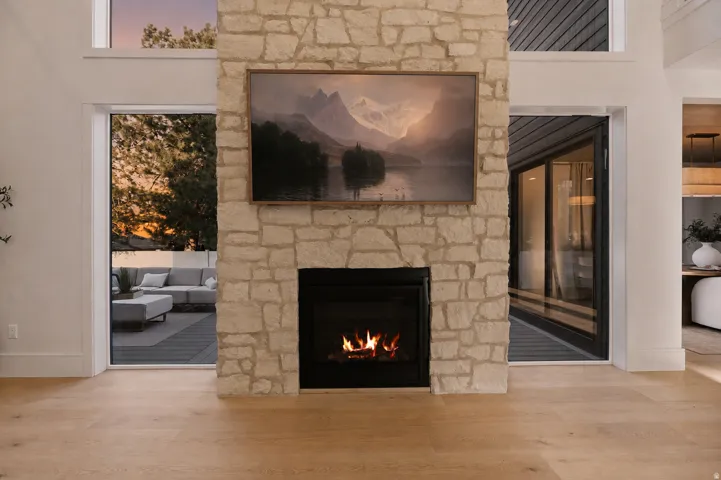 Floor-to-ceiling stone fireplace with a black firebox, light-toned wood-finish flooring, and expansive glass doors opening to an outdoor deck