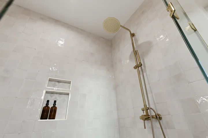 White tiled shower surround with dual recessed niches and brass-finish fixtures