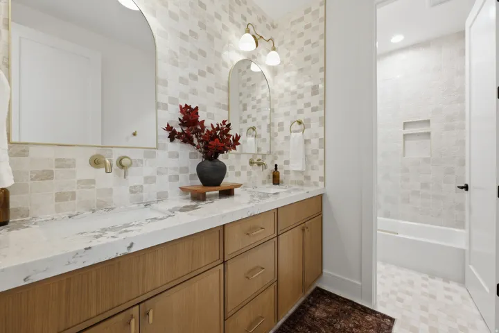 Dual vanity with integrated sinks, stone countertop, wood-finish cabinetry, arched mirrors, and wall-mounted faucets