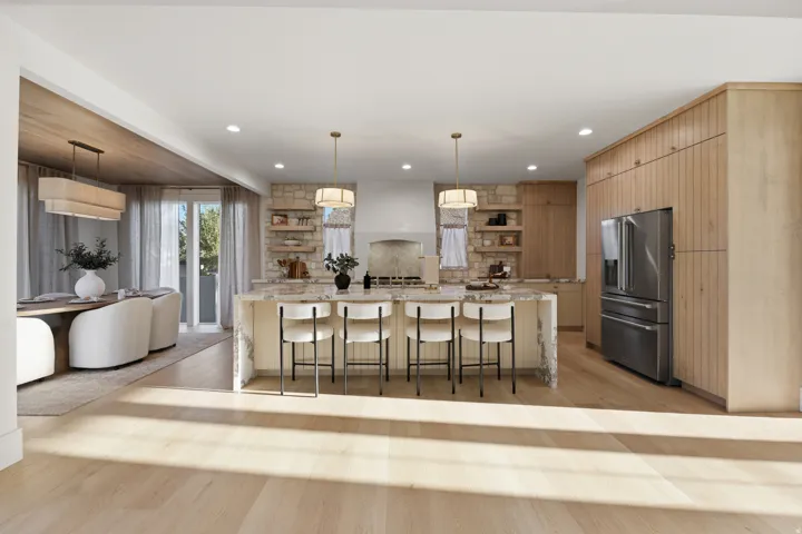 Open-concept kitchen with wood-finish flooring, stone accent wall, and built-in stainless steel refrigerator