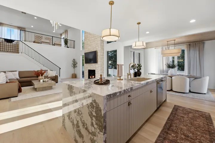 Open-concept living space with a large kitchen island, light wood-finish flooring, and a stone-clad fireplace