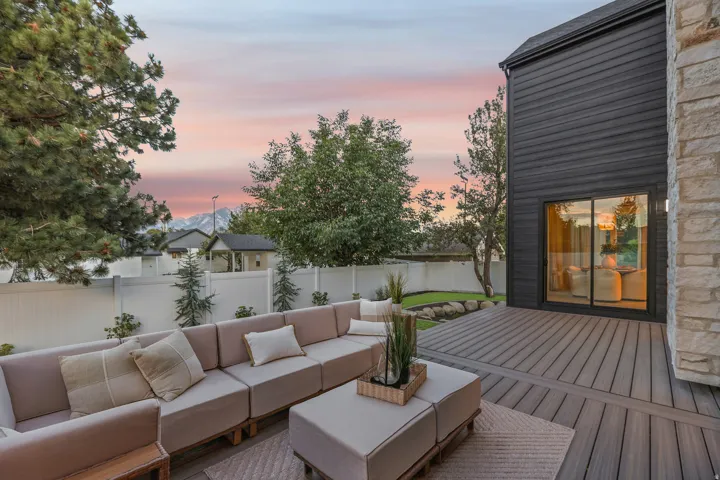 Expansive exterior deck with composite decking, featuring a sliding glass door entry to the interior, dark horizontal siding, and natural stone accents
