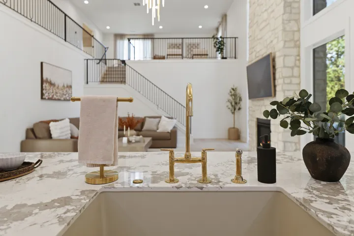 Kitchen sink with a gold-finish faucet, stone-look countertop, and an open-concept living area with a stone fireplace