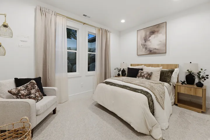 Recessed lighting, light-toned carpeting, two windows with curtain rods, and a wood-finish headboard