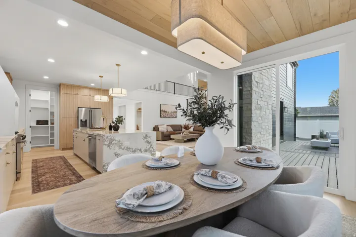 Wood-finish ceiling with a statement chandelier, wood-finish flooring, built-in kitchen cabinetry, and an expansive sliding glass door opening to a deck