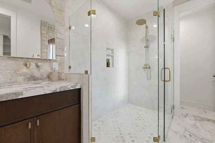 Walk-in shower with clear glass enclosure, brass fixtures, and a tiled shower niche