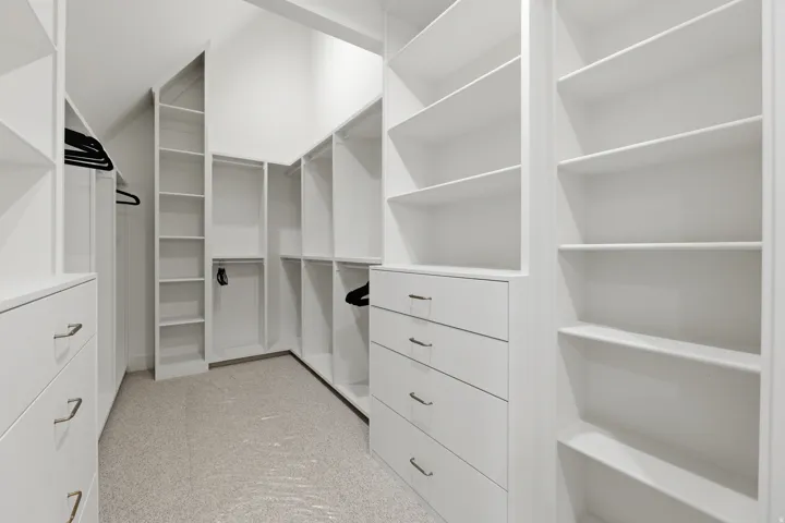 White custom closet system featuring multiple shelving units and built-in drawers with polished hardware