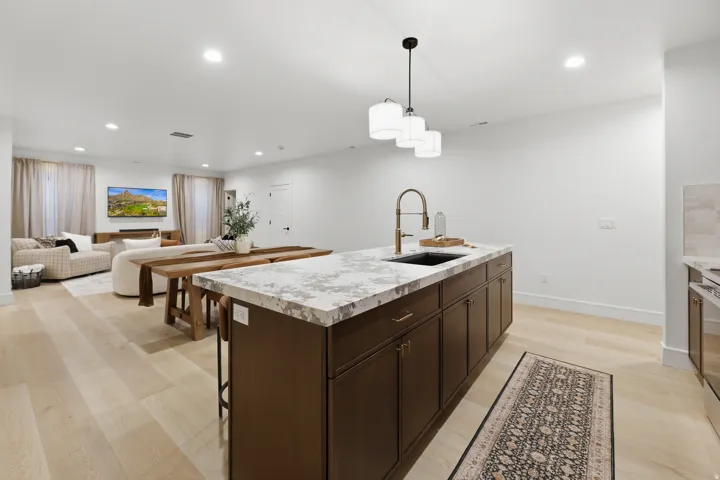 Open-concept living space with light wood-finish flooring, a kitchen island featuring a light-toned countertop, dark cabinetry, and a bronze-finish faucet