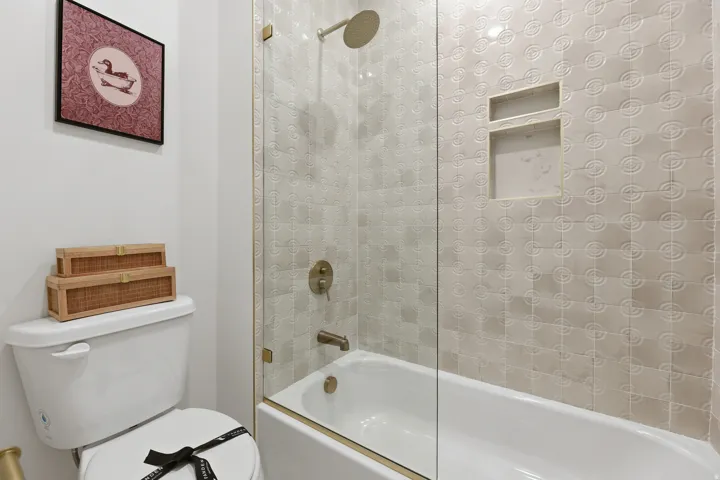 Bathtub with a glass shower enclosure, textured tile surround, built-in shower niches, and a shower head with matching fixtures