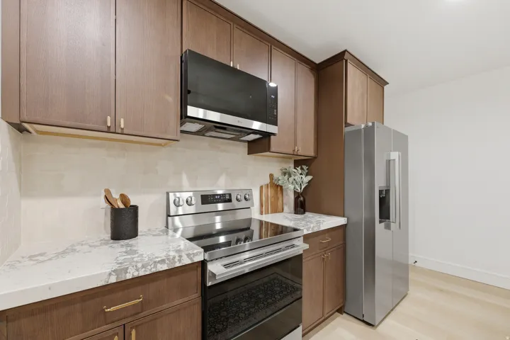Kitchen featuring stainless steel appliances, wood-finish cabinetry, light-toned wood-finish flooring, and white countertops
