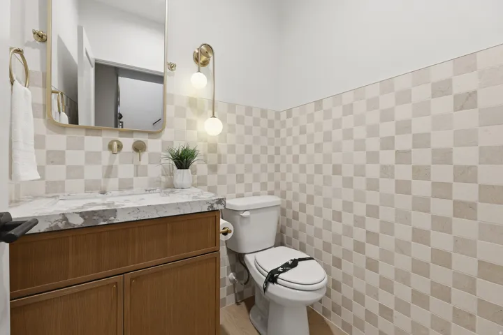 Powder room with a wood-finish vanity, stone countertop with integrated sink, gold-tone hardware, and checkerboard wall tile