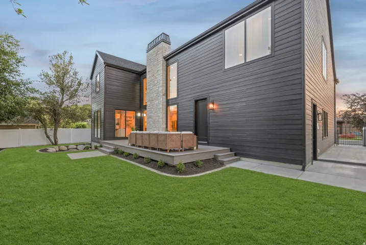 Expansive green space featuring a multi-level wood-finish deck with integrated lighting, a stone-clad chimney, and dark horizontal siding