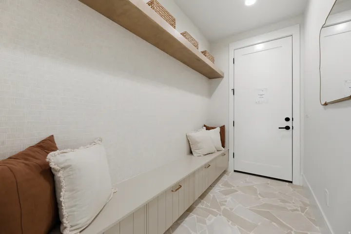 Built-in bench with storage, wood-finish floating shelf, white paneled door with black hardware, and patterned floor tile