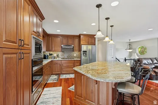 Cherry wood cabinetry with stainless steel appliances, granite countertops, and a  tile backsplash