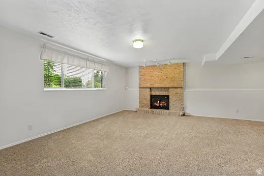 Brick-faced fireplace with hearth, track lighting, and a large window with blinds