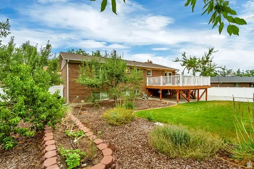 Brick exterior with an elevated composite wood deck, white railing, and an expansive lawn
