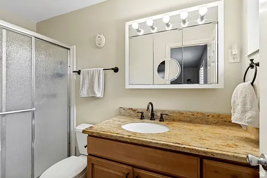Primary bathroom, enclosed shower with frosted glass doors, a Cherry vanity with a granite countertop, a built-in medicine cabinet with integrated lighting, and dark-finished fixtures