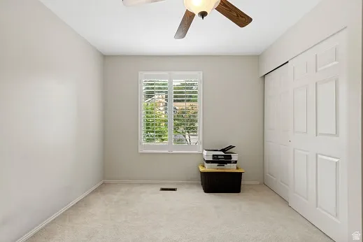 2nd bedroom, used as an office, neutral tone walls, light-colored carpet flooring, ceiling fan with light fixture, and white sliding closet doors