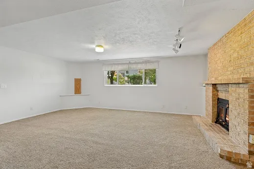 Expansive room featuring a brick fireplace with a hearth, wall-to-wall carpeting, and a window with blinds