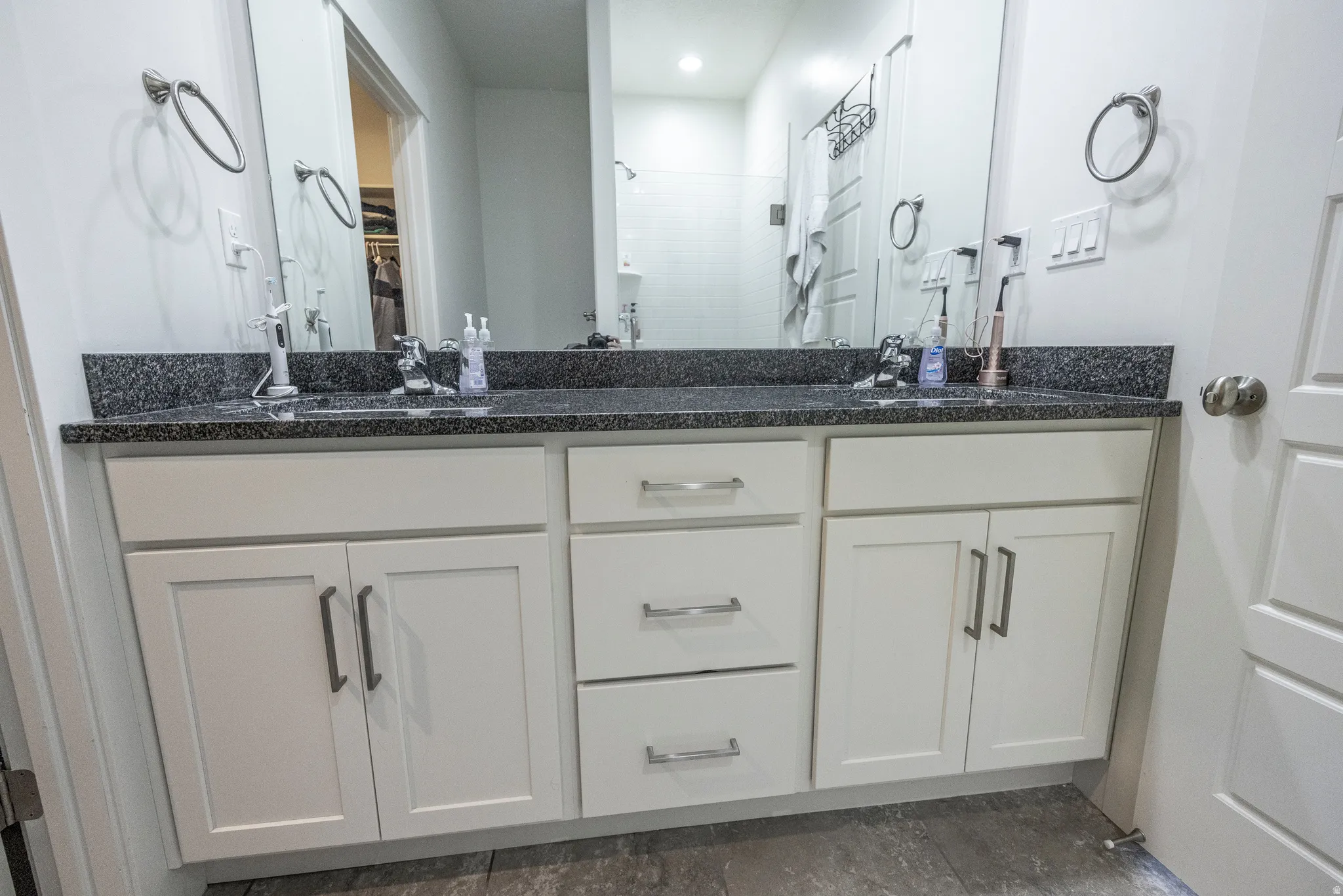 Dual vanity with white cabinetry, dark speckled countertop, and chrome fixtures