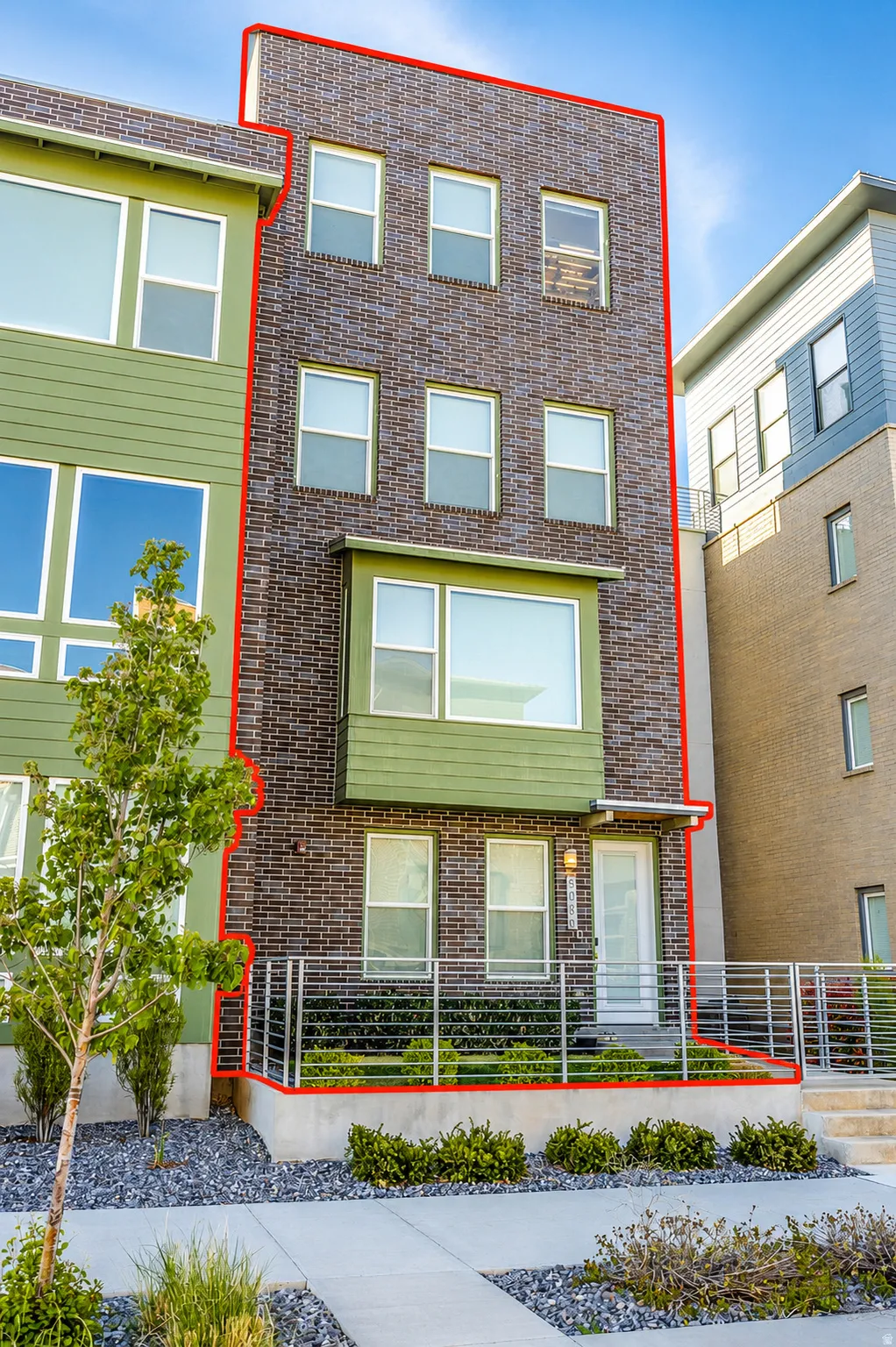 Multistory facade featuring brick and siding, multiple windows, a prominent bay window, and a ground-level entrance with a railing
