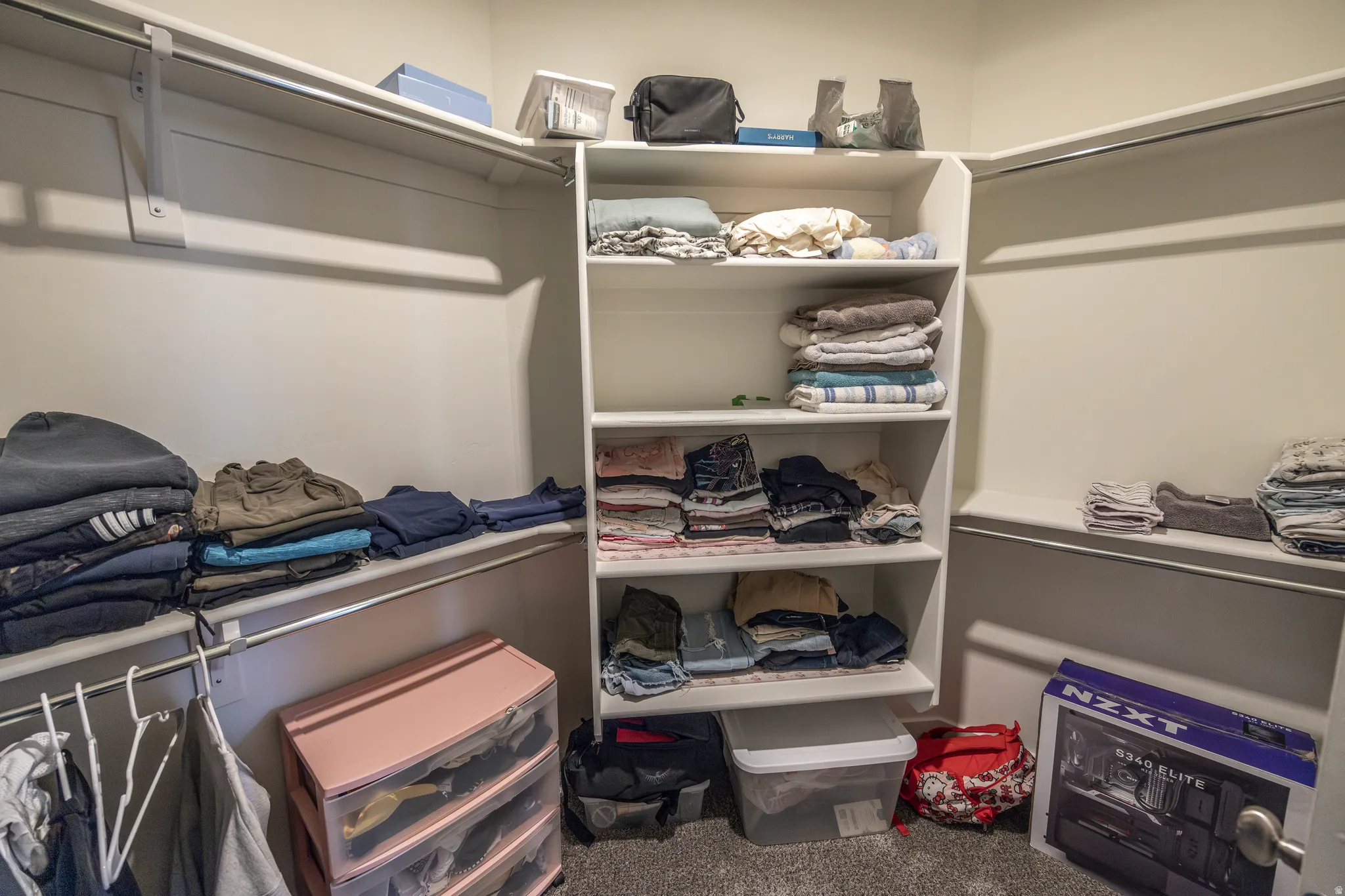 Walk-in closet featuring white built-in shelving, hanging rods, and carpet flooring