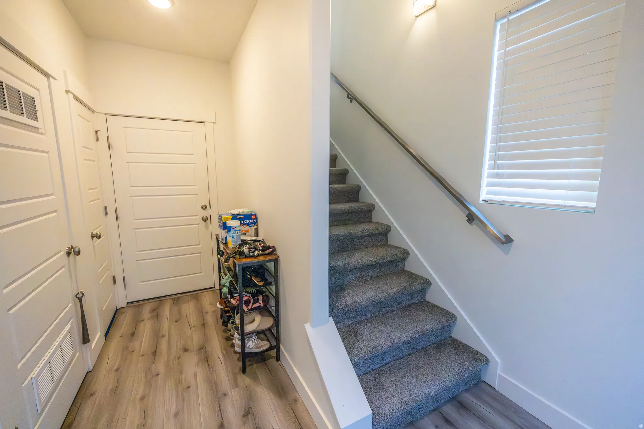 Light-toned wood-finish flooring, white paneled doors, and a carpeted staircase with a metal handrail