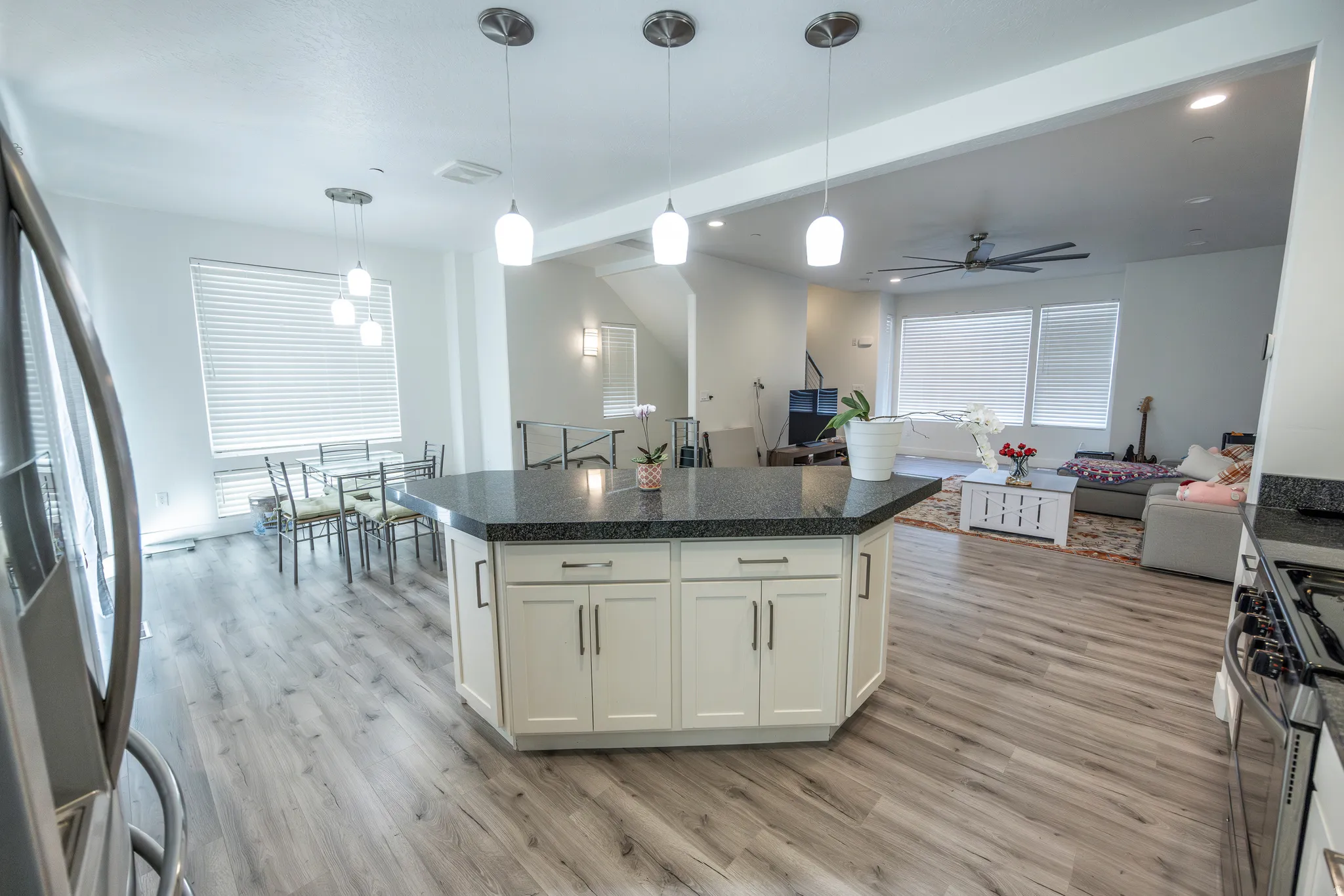 Kitchen island with dark countertop and white cabinetry, recessed lighting, wood-finish flooring, and white window blinds