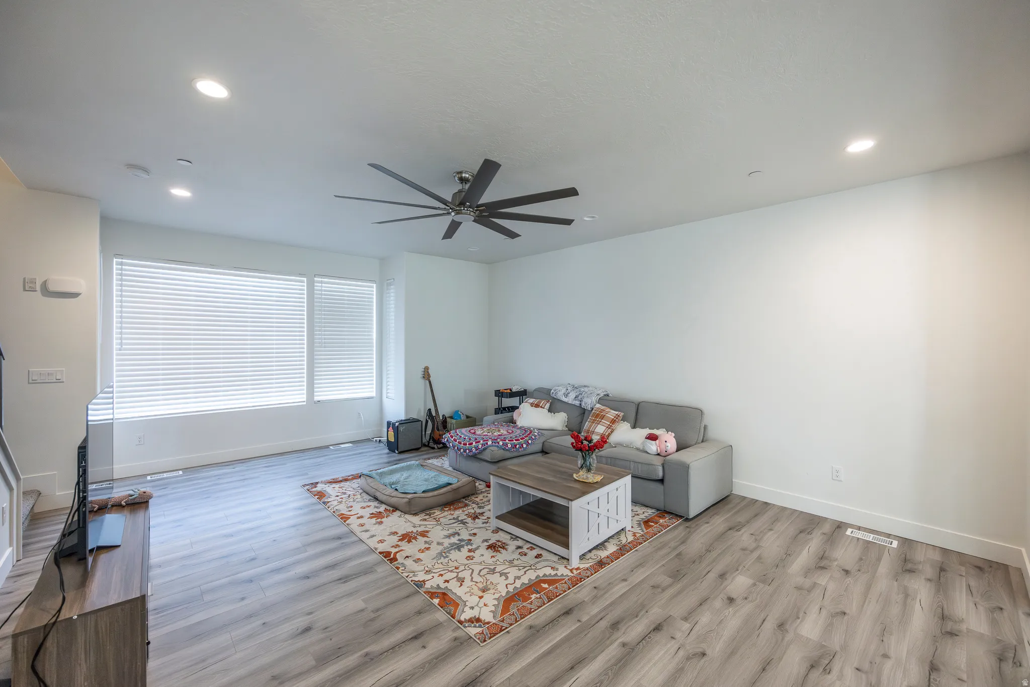 Wood-finish flooring, recessed lighting, ceiling fan, and multiple windows with blinds