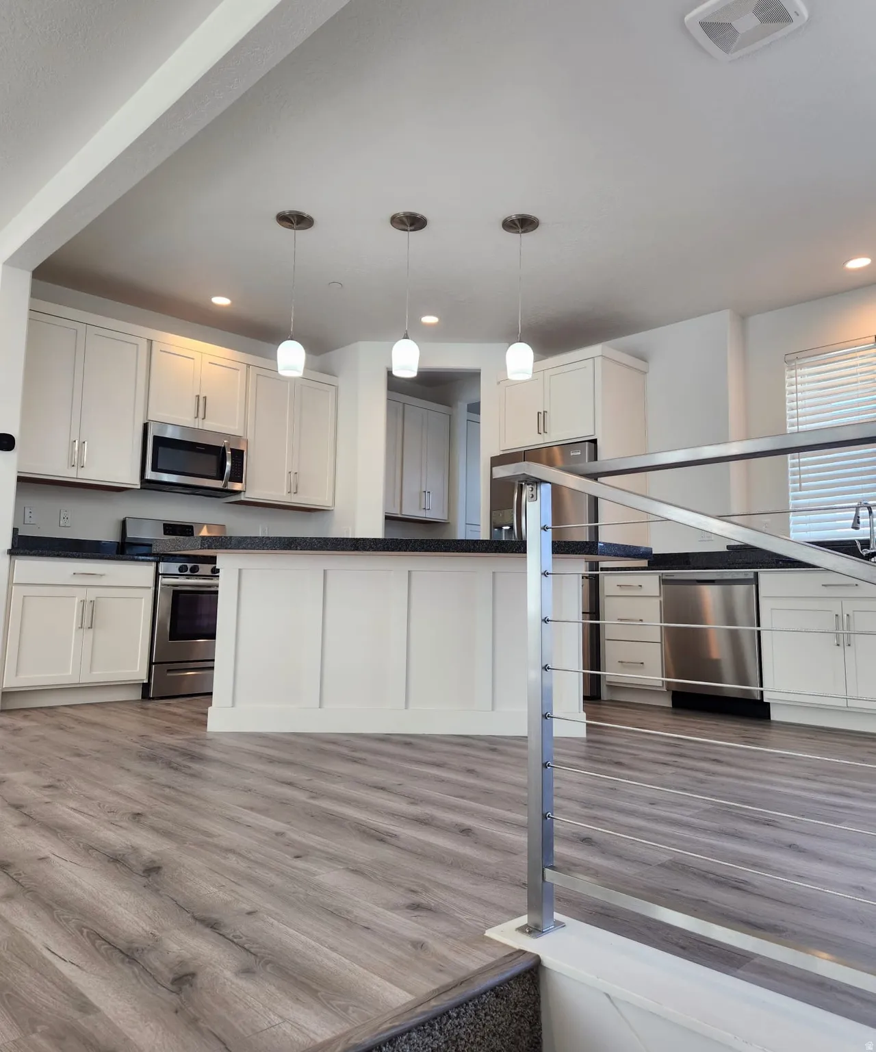 Kitchen featuring white cabinetry, dark countertops, stainless steel appliances, and pendant lighting