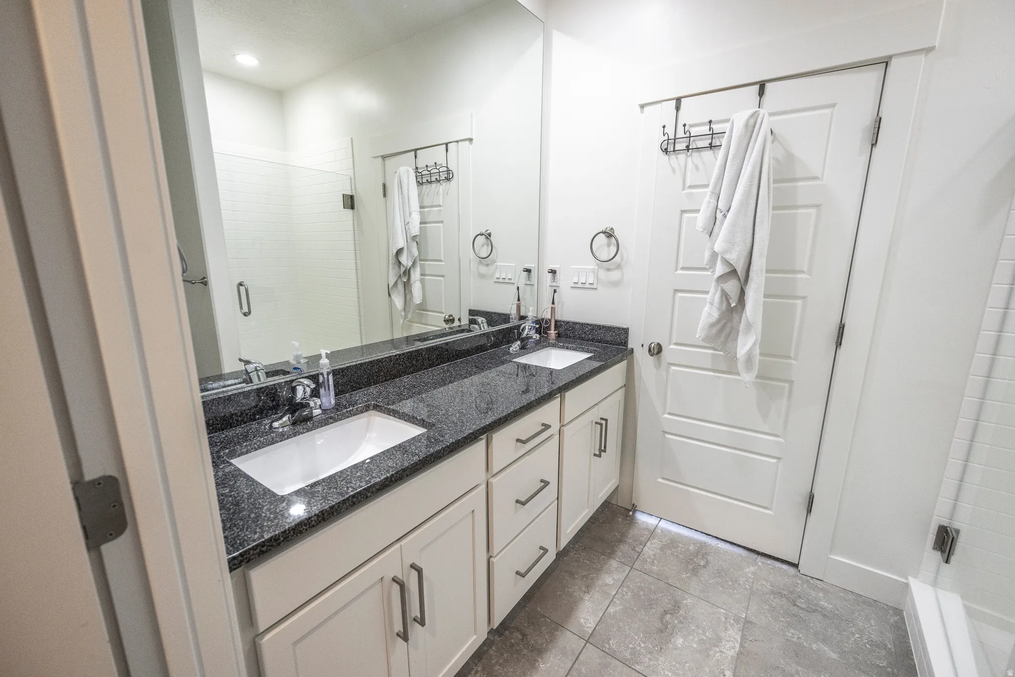 Dual vanity with dark stone countertop, undermount sinks, and white cabinetry