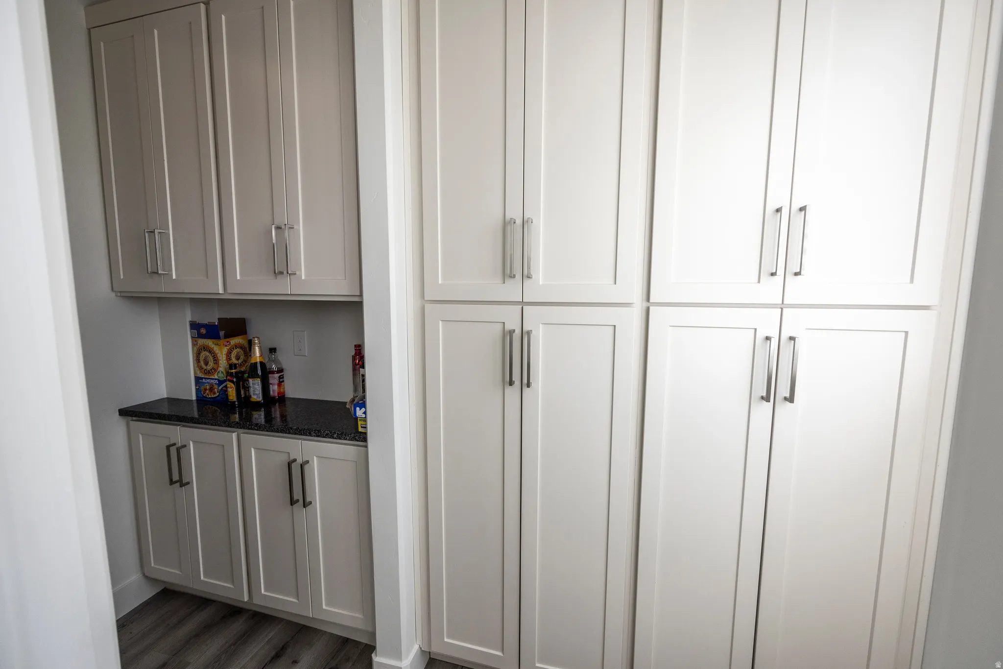 Built-in cabinetry with shaker-style doors, black countertop, white walls, and wood-finish flooring