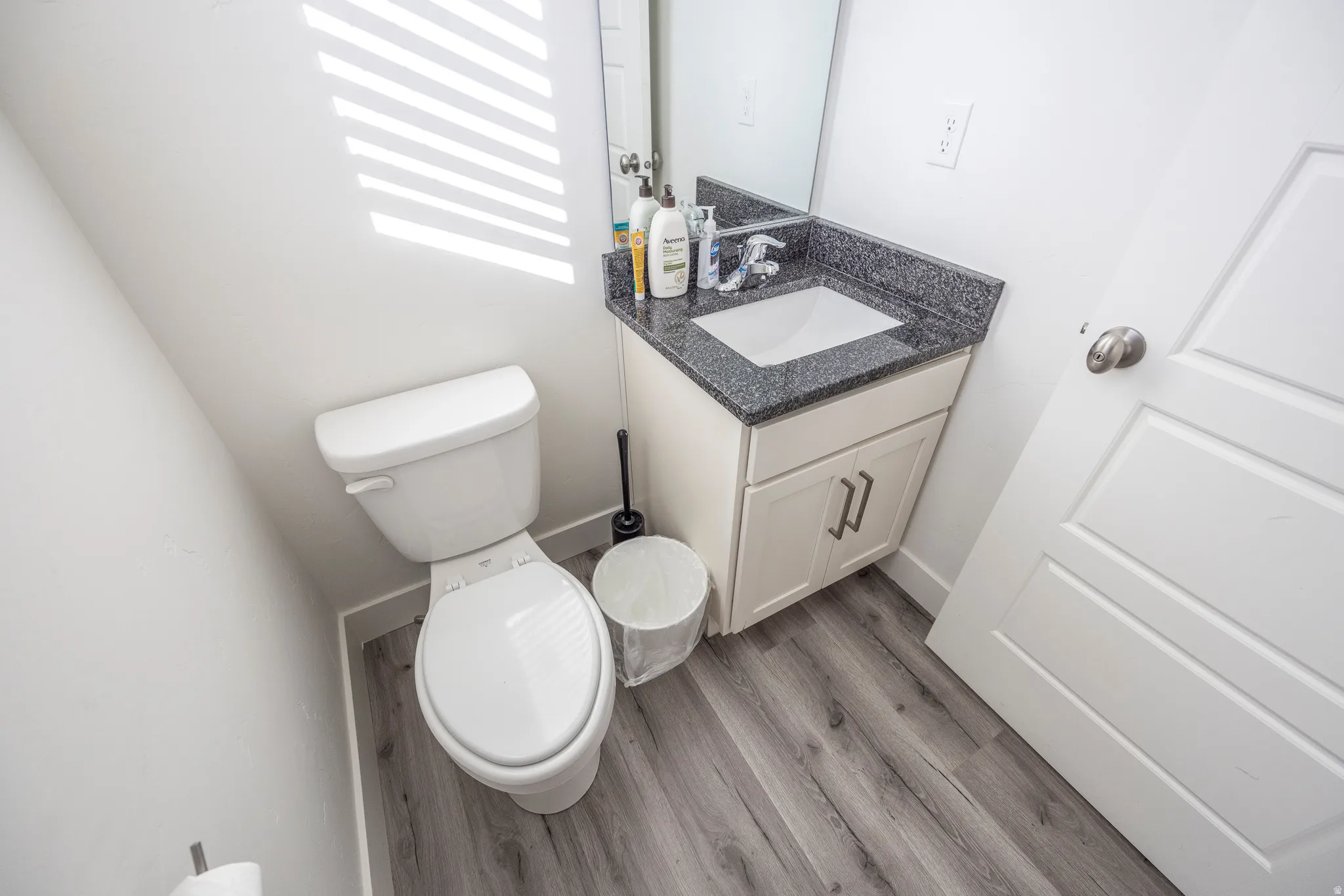 Half bath on the 2nd floor  featuring a white toilet, wood-finish flooring, a vanity with a white basin and dark countertop, and a mirror