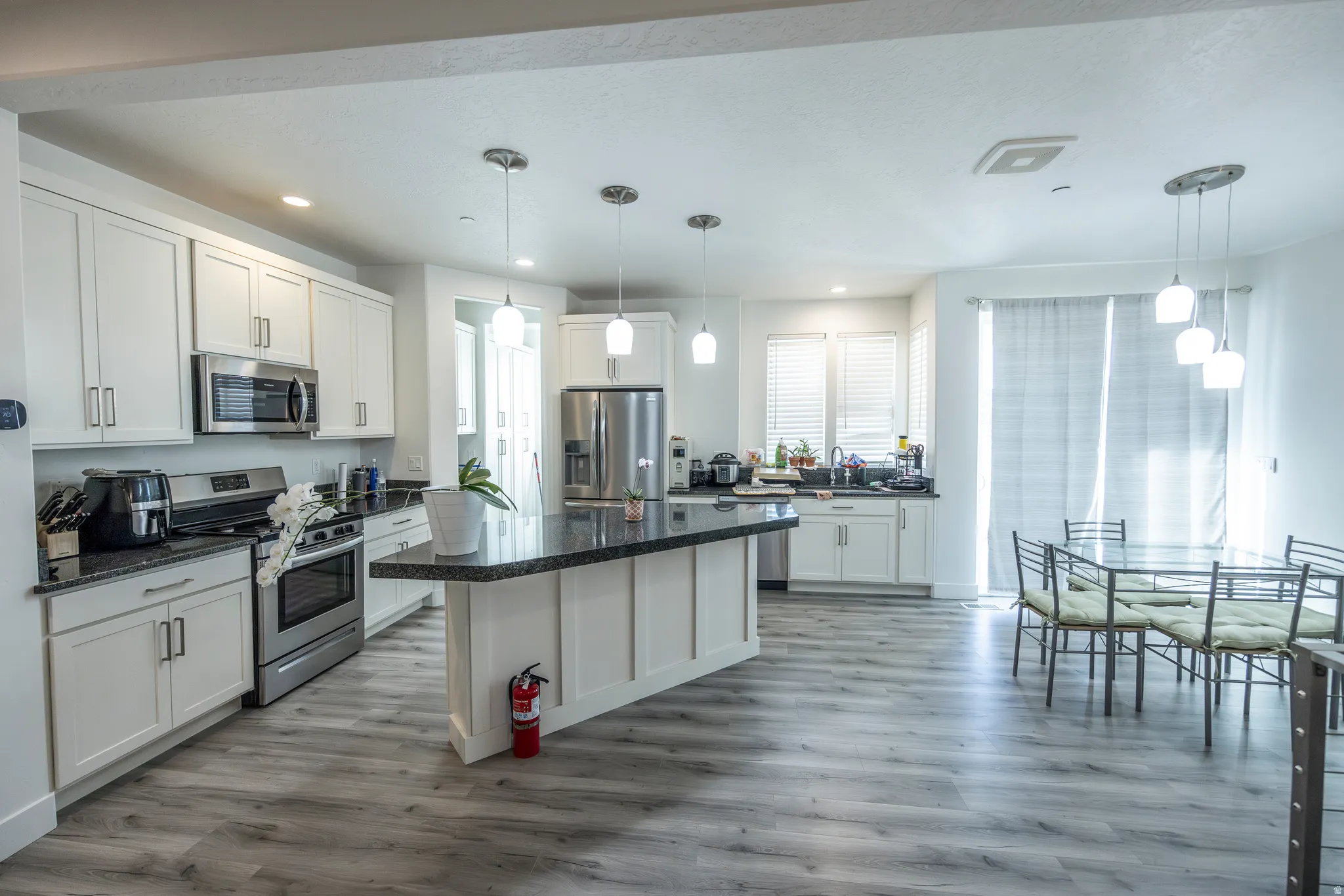 Open-concept kitchen featuring white cabinetry, stainless steel appliances, dark countertops, and wood-finish flooring