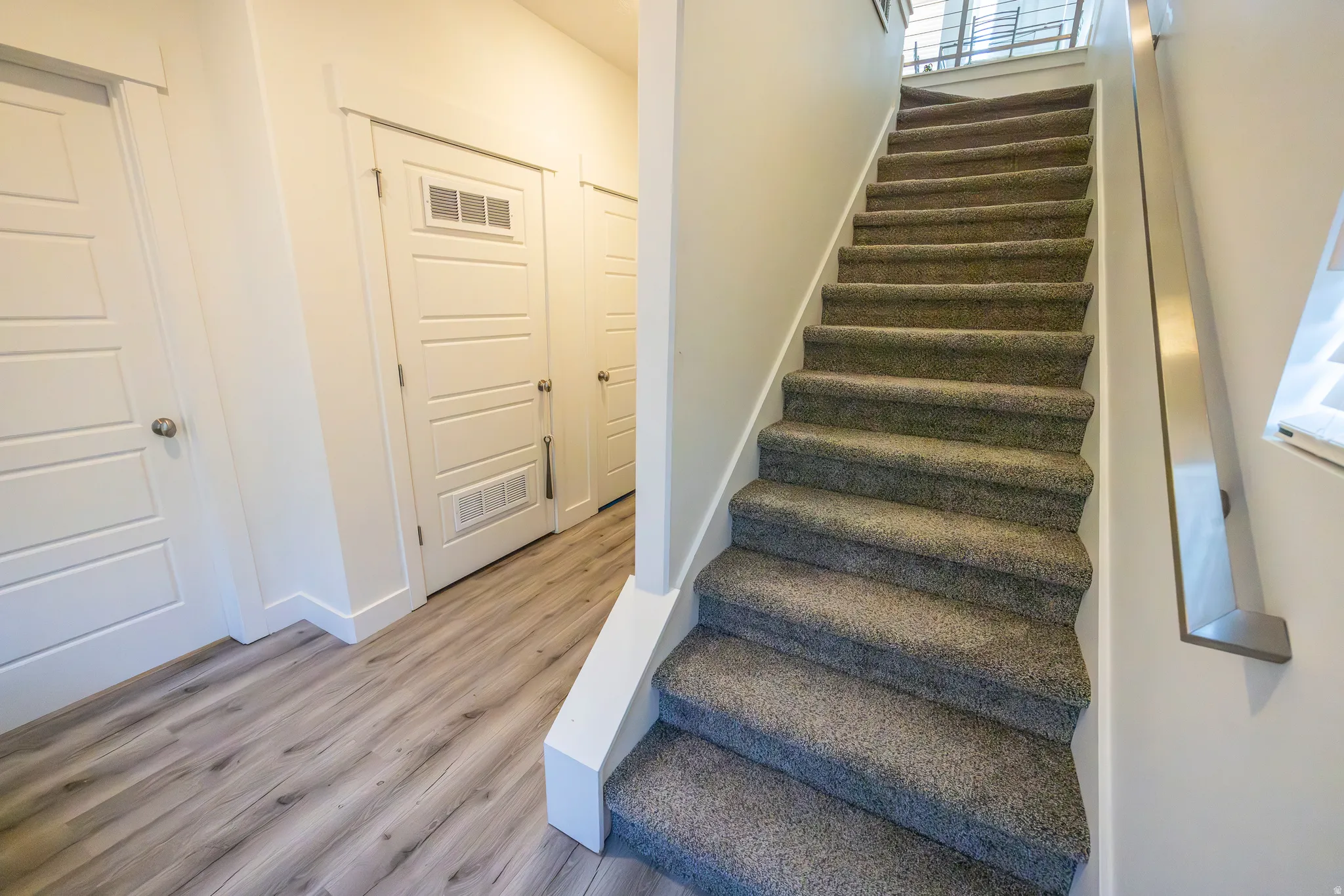 Carpeted staircase with a metal handrail, wood-finish flooring, and white paneled doors
