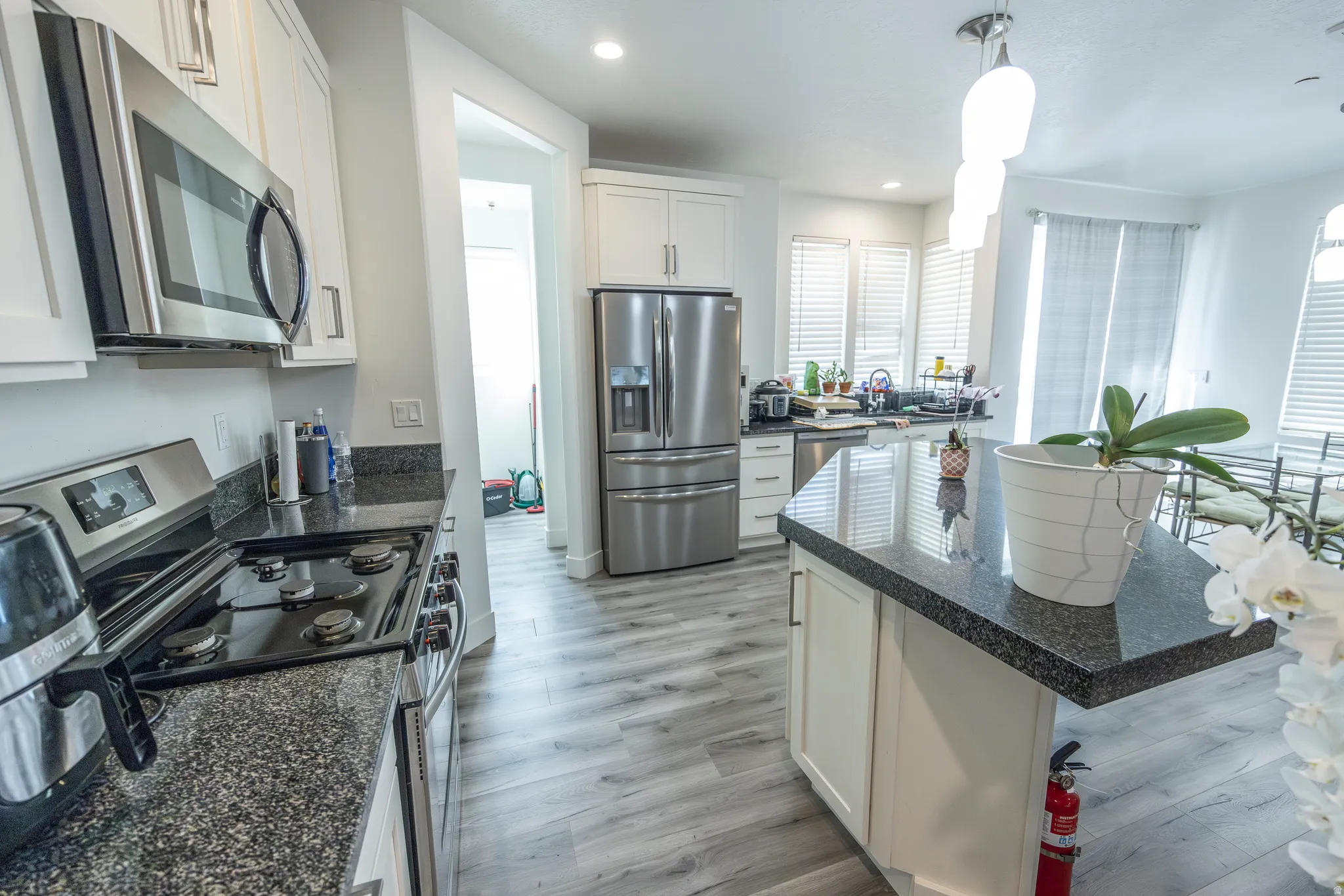 Kitchen featuring stainless steel appliances, white cabinetry, dark speckled countertops, a center island with countertop seating, and wood-finish flooring