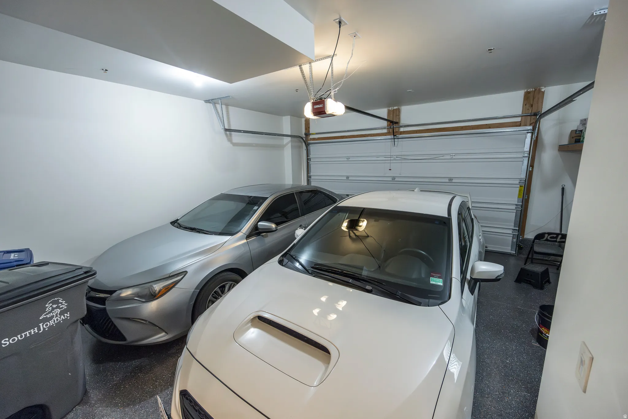 Spacious two-car garage featuring polished concrete flooring, overhead storage systems, and ample natural lighting from recessed ceiling fixtures and garage door windows
