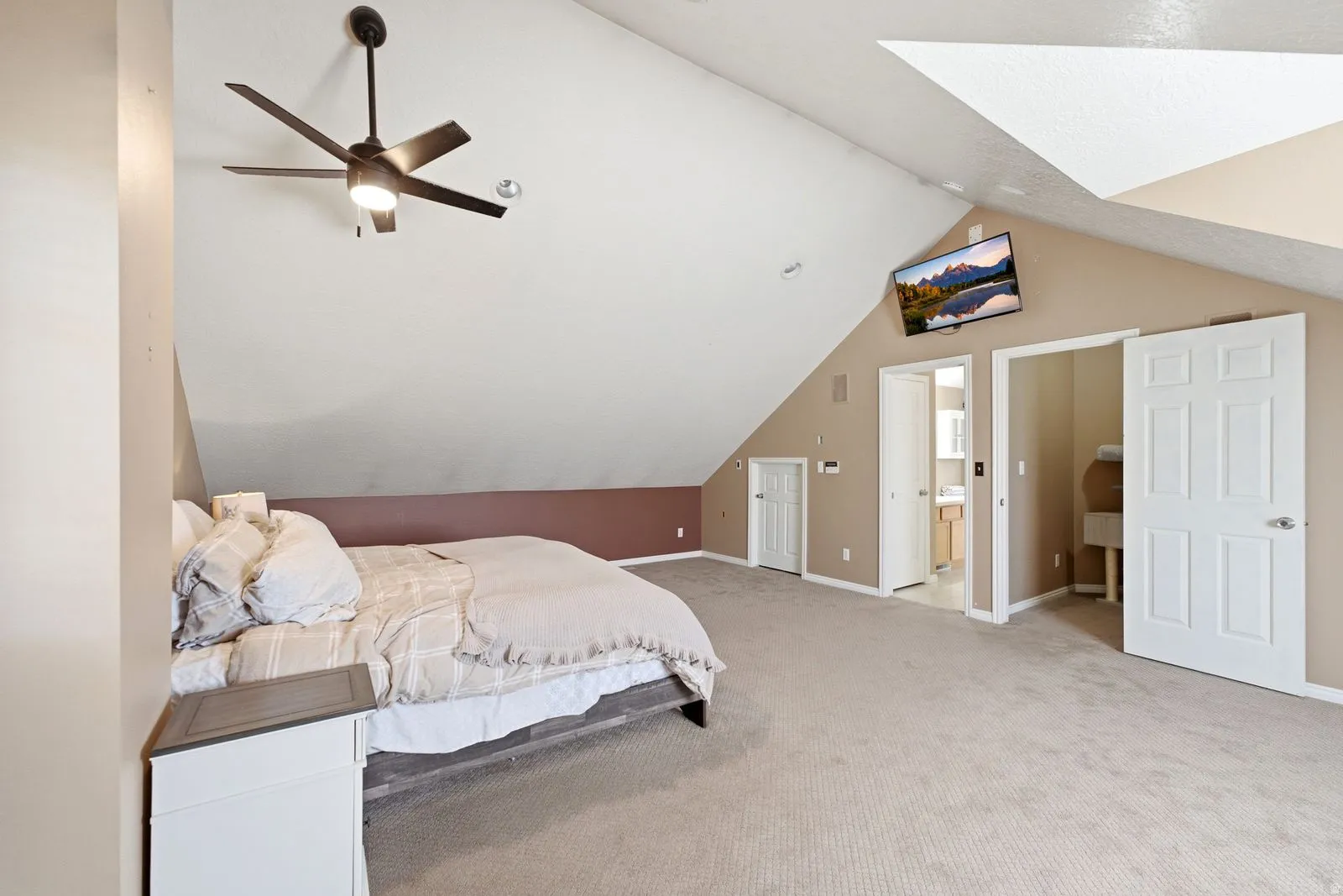 Vaulted ceiling with skylight, ceiling fan, carpeted flooring, and paneled interior doors