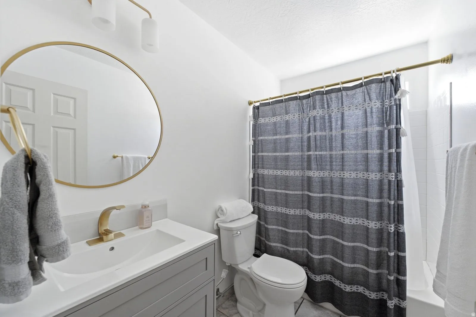 Vanity with a single basin, gold-finish faucet, and round mirror