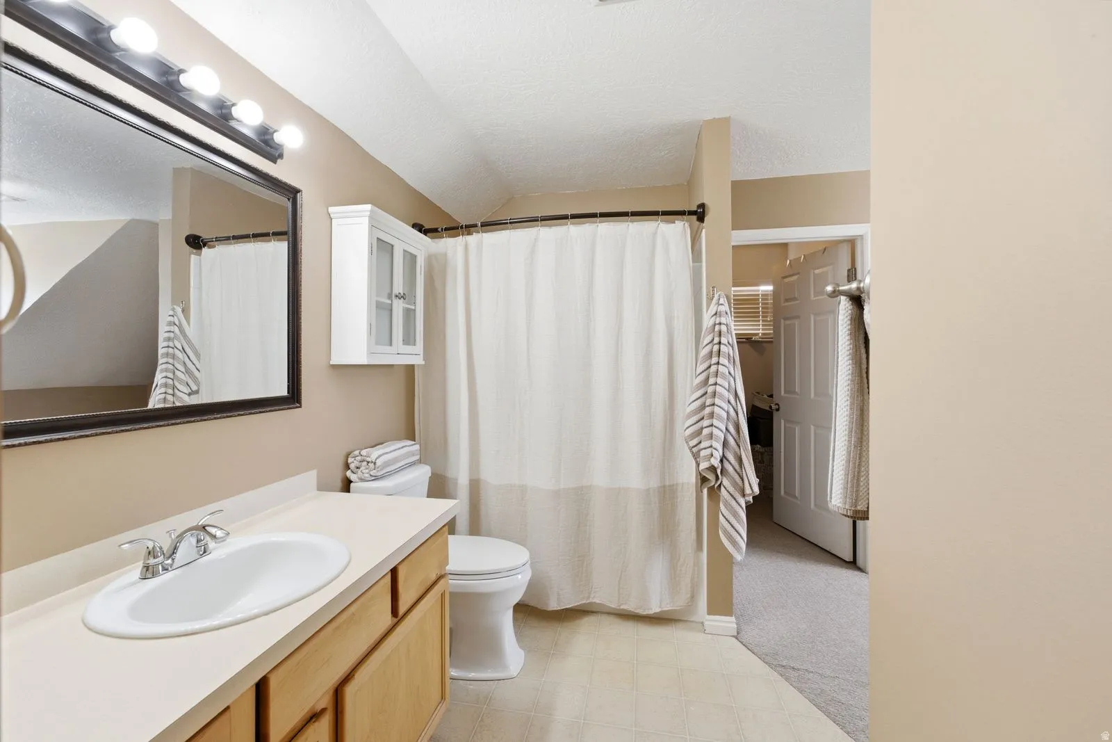 Bathroom featuring a light wood-finish vanity with an integrated sink, a framed mirror, an overhead vanity light, a white wall-mounted cabinet, and a shower/tub combination
